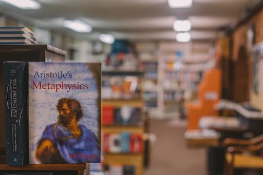 Aristotle’s Metaphysics is shown in the foreground, with a bookstore or library blurred in the background
